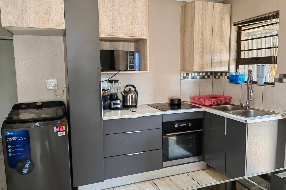 Compact modern kitchen featuring two-tone cabinetry, integrated oven and hob, stainless steel sink, and tiled backsplash.