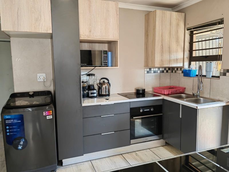Compact modern kitchen featuring two-tone cabinetry, integrated oven and hob, stainless steel sink, and tiled backsplash.
