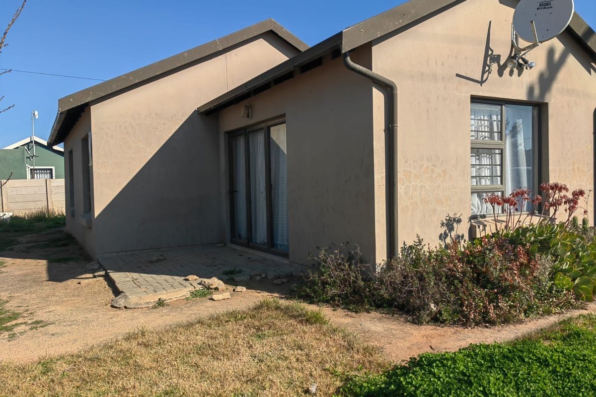 Rear exterior view of the house featuring a paved patio area, sliding glass doors, and established garden beds.