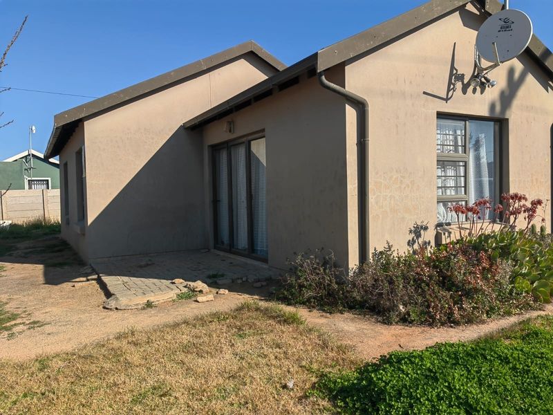 Rear exterior view of the house featuring a paved patio area, sliding glass doors, and established garden beds.