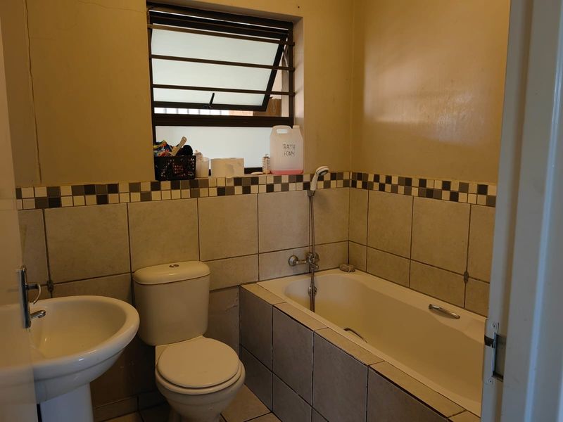 A compact bathroom featuring a pedestal basin, toilet, and bathtub with a tiled splashback and security-barred window.