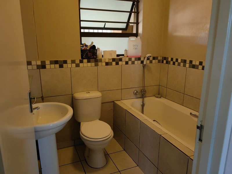 A functional bathroom featuring a pedestal basin, toilet, and a tiled built-in bathtub with a handheld shower mixer.