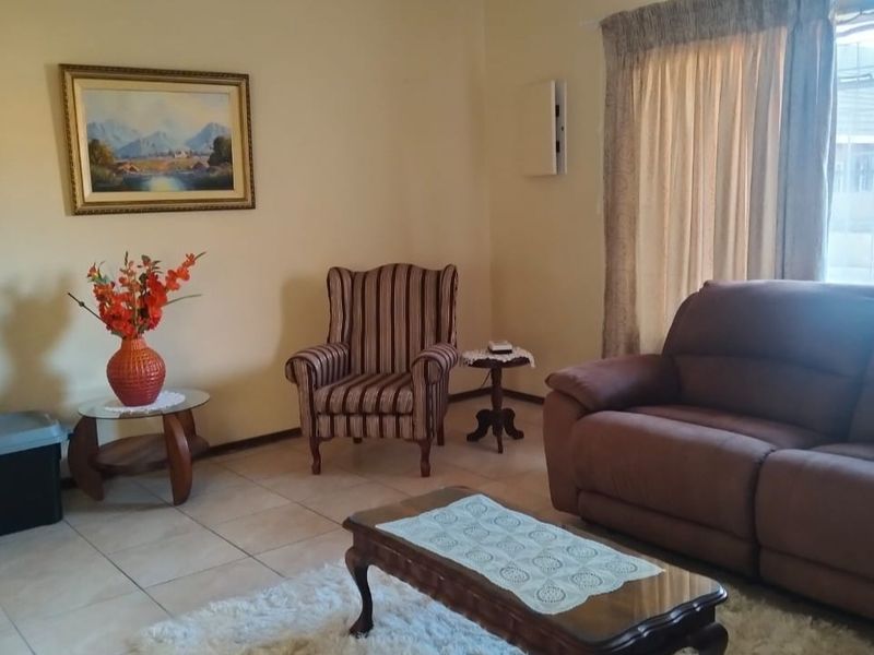 A comfortable living room featuring tiled flooring and large windows with curtain rails, providing a functional and well-lit space.