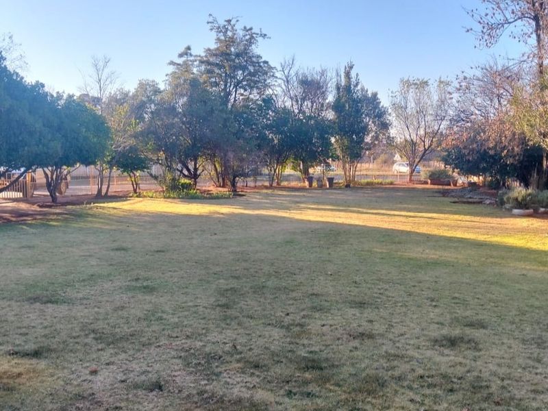 A spacious, well-established garden featuring a large lawn area surrounded by mature trees and perimeter fencing.