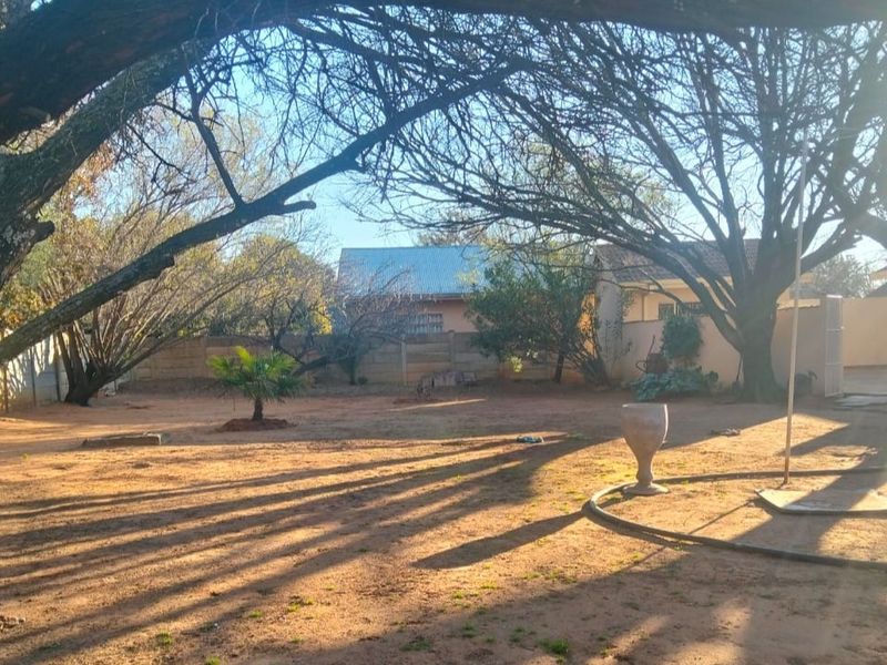 A spacious backyard area featuring mature trees and a precast concrete boundary wall, offering a blank canvas for landscaping.