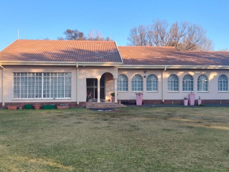 A single-story residential home featuring a tiled roof, arched windows, and a covered entrance, set against a large lawn area.