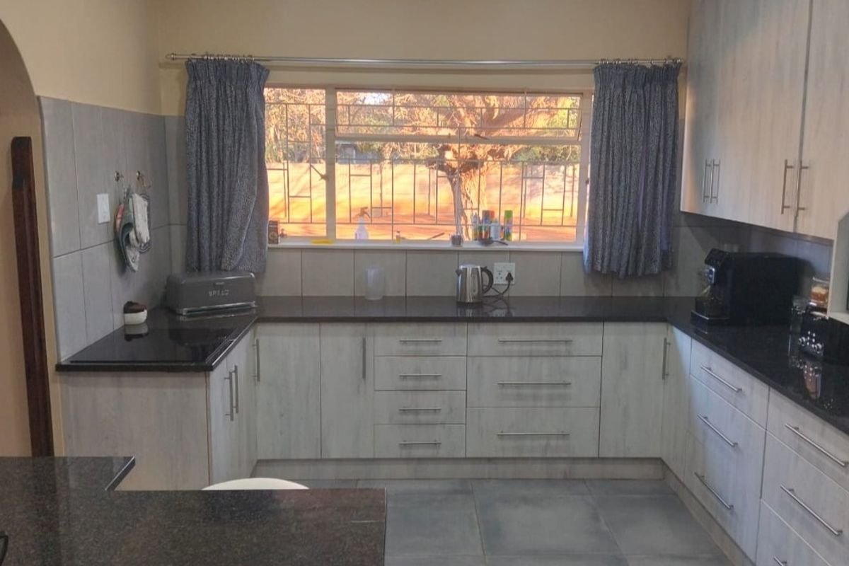 A functional kitchen featuring light-toned cabinetry, dark granite countertops, tiled backsplash, and tiled flooring with a window overlooking the exterior.