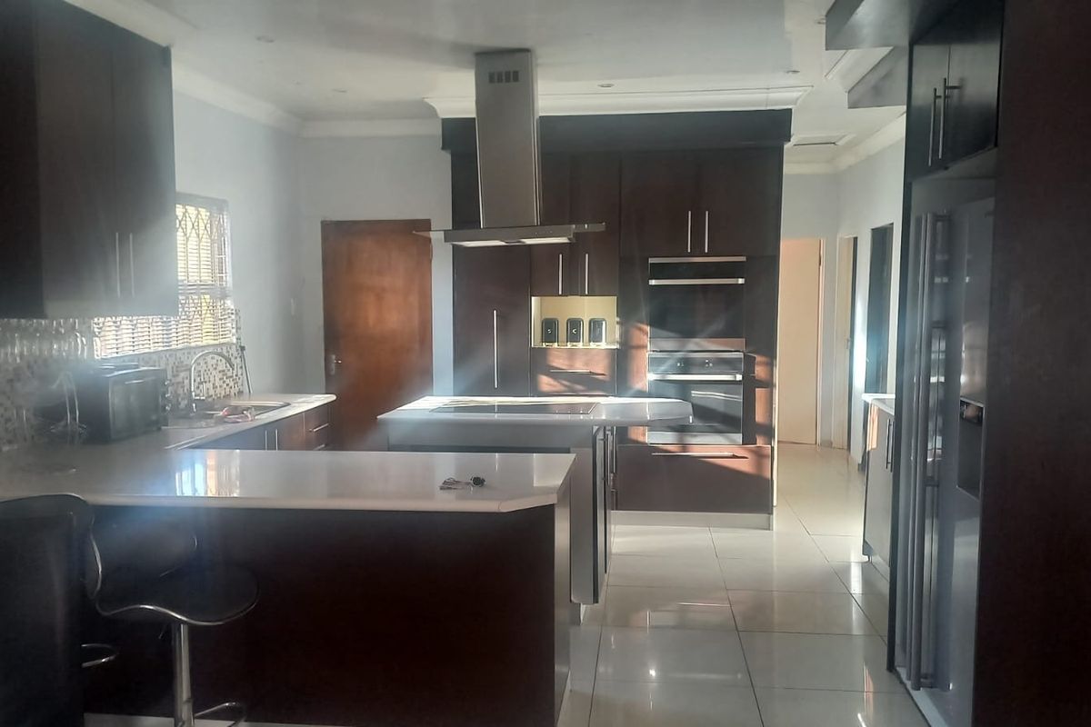 Modern kitchen featuring dark wood cabinetry, stone countertops, a central island, built-in double oven, and stainless steel extractor fan with tiled flooring.