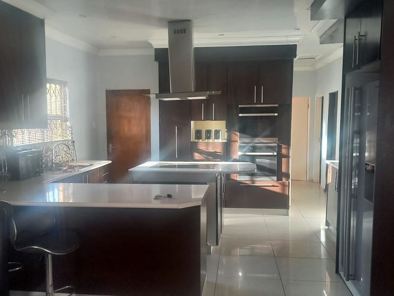 Modern kitchen featuring dark wood cabinetry, stone countertops, a central island, built-in double oven, and stainless steel extractor fan with tiled flooring.