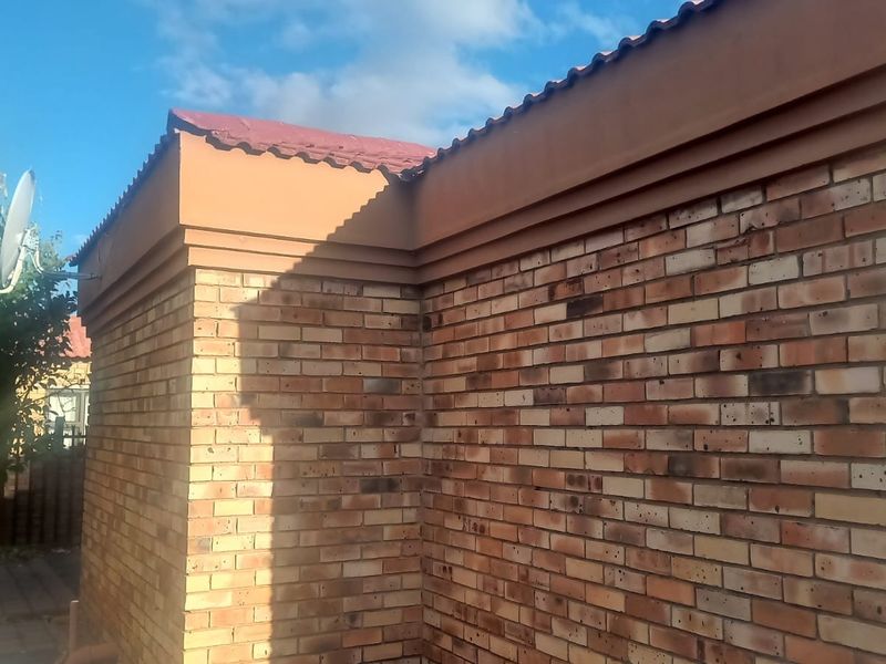 A view of the exterior rear face brick wall and tiled roof structure of the house.