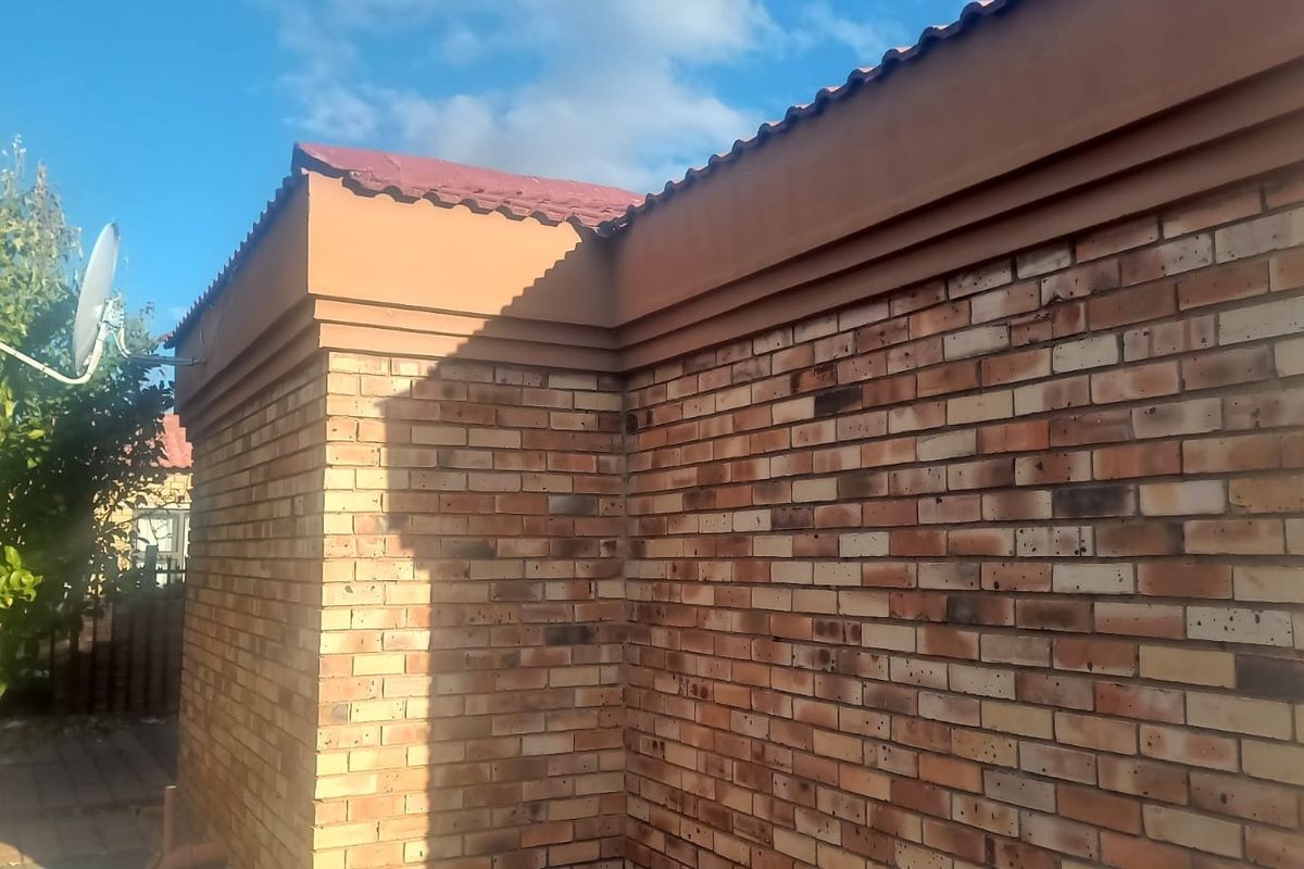A view of the exterior rear face brick wall and tiled roof structure of the house.