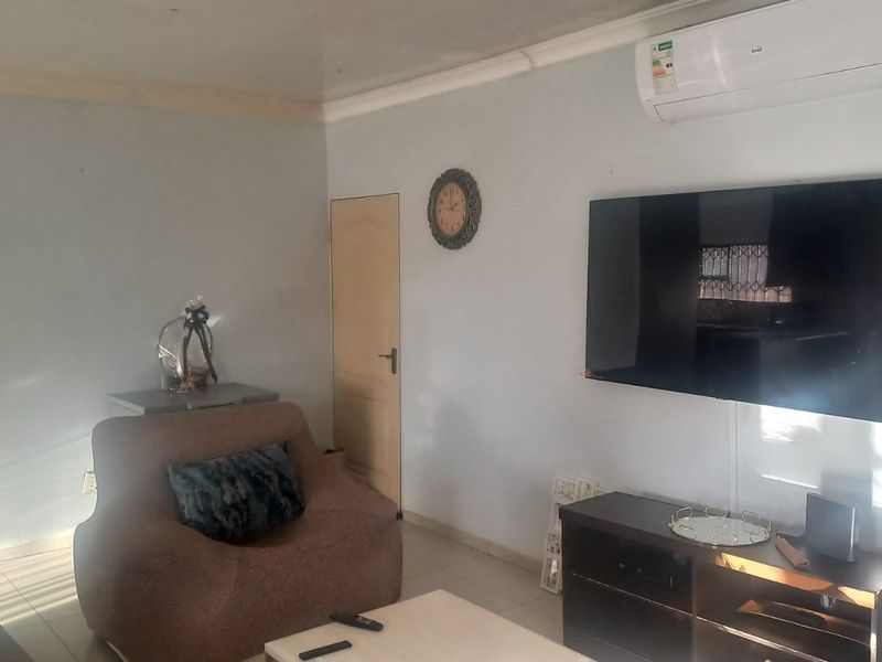 A living room featuring tiled flooring, coving, and a wall-mounted split-system air conditioner.