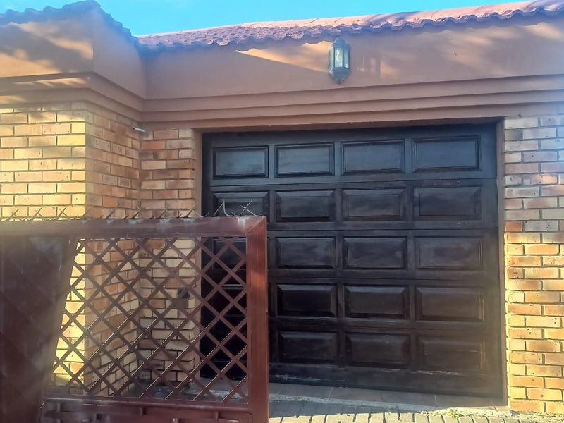 Exterior view of a residential garage featuring a dark sectional door, brick masonry, and a tiled roof with an integrated security gate.