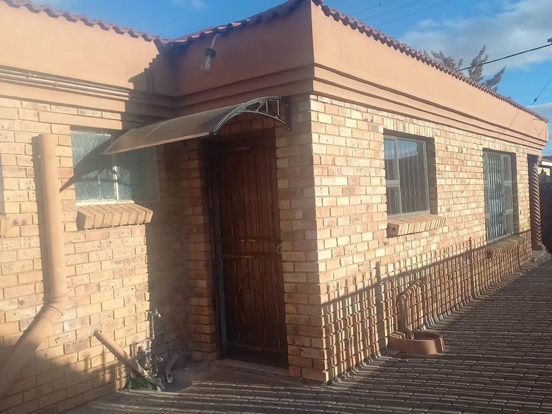 A single-story face brick house exterior featuring a paved driveway, security gate, and protective window bars.