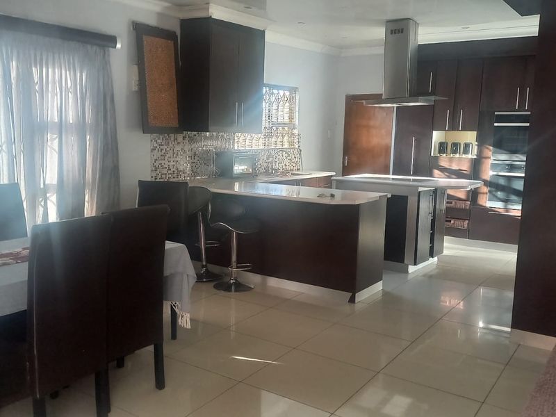 Spacious open-plan kitchen and dining area featuring dark wood cabinetry, a central island with an extractor fan, and modern tiled flooring.