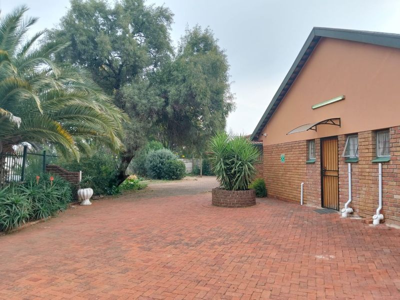 A paved rear courtyard area featuring facebrick exterior walls, a security gate, and established garden landscaping.