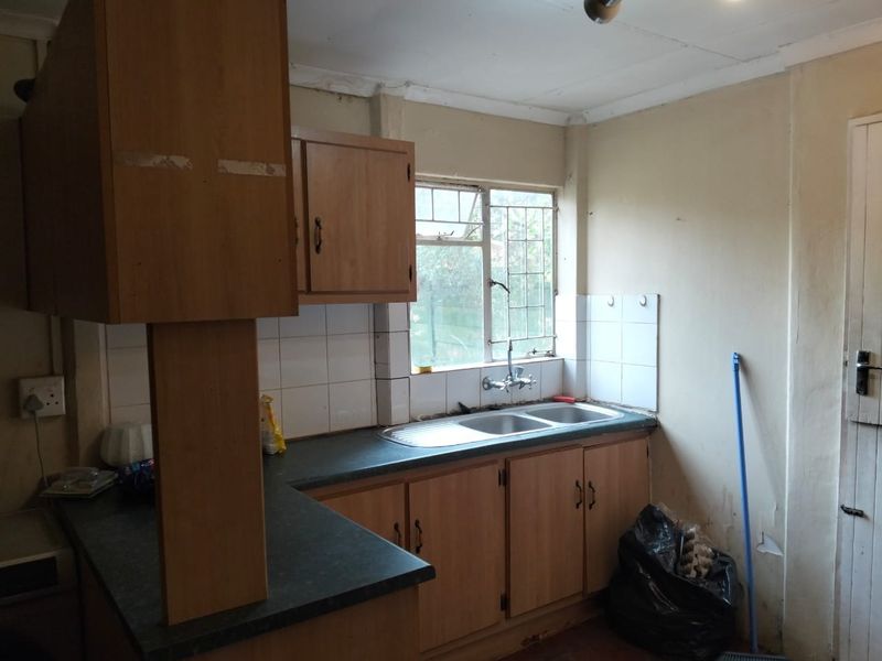 A dated kitchen featuring laminate cabinetry, a double bowl sink, and tiled splashbacks, requiring cosmetic updates and repairs to wall finishes.