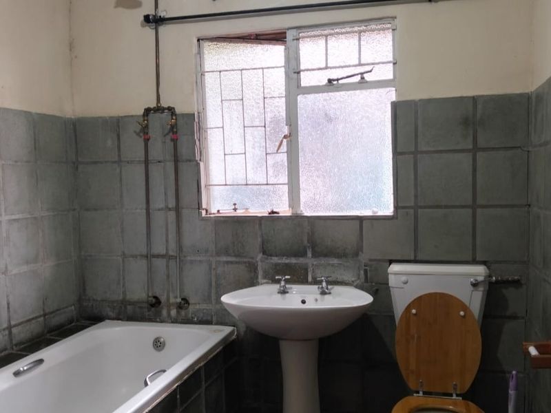 A dated bathroom featuring a pedestal basin, bathtub, and toilet with original wall tiling and exposed plumbing fixtures.