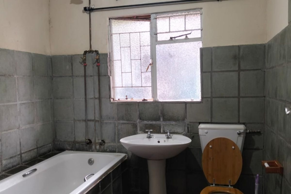A dated bathroom featuring a pedestal basin, bathtub, and toilet with original wall tiling and exposed plumbing fixtures.