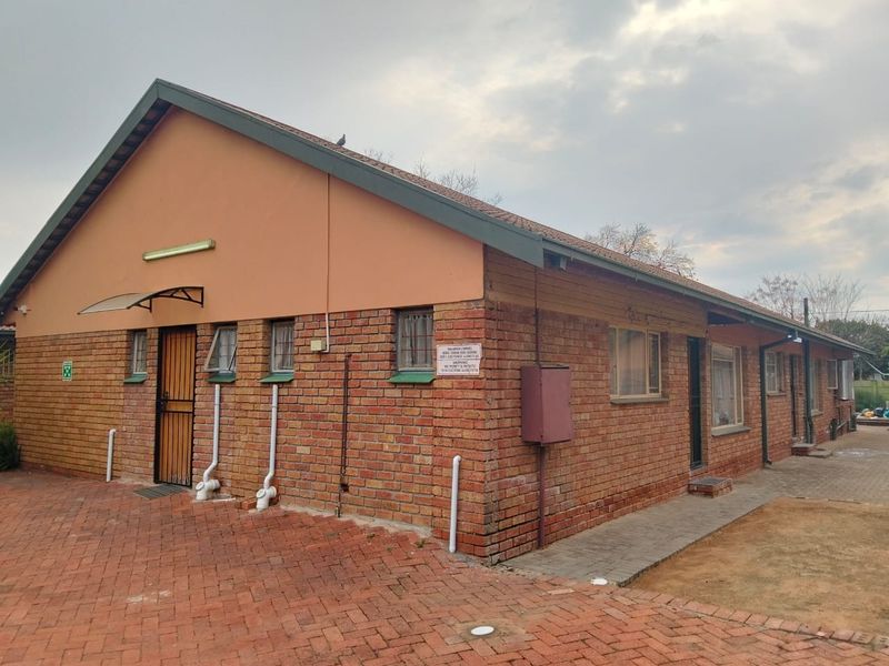 Rear view of a face brick house featuring a pitched roof, paved exterior area, and security access points.