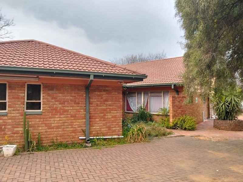 Rear view of a brick house featuring a tiled roof, paved driveway, and established garden area.