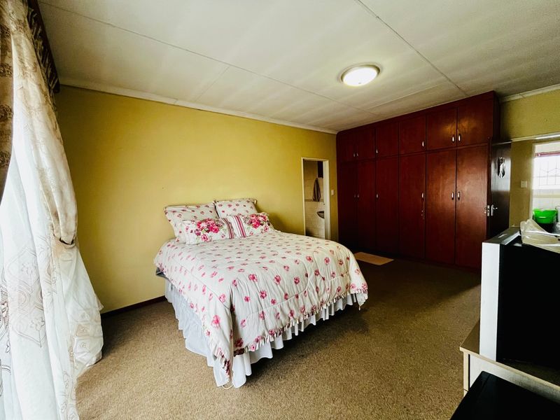 Spacious bedroom featuring extensive built-in wooden cupboards, carpeted flooring, and direct access to an en-suite bathroom.