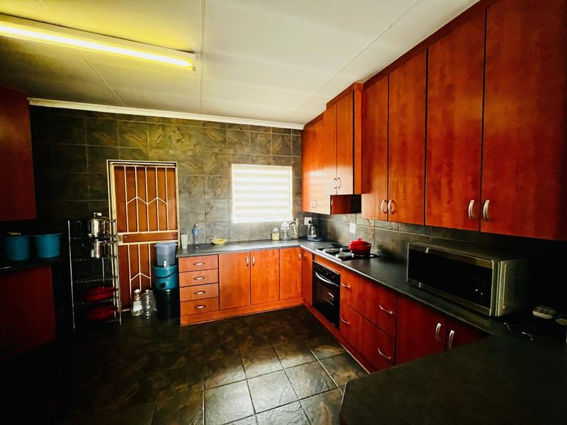 A functional kitchen featuring warm-toned wooden cabinetry, dark tiled flooring, a built-in oven and hob, and a secure access door.
