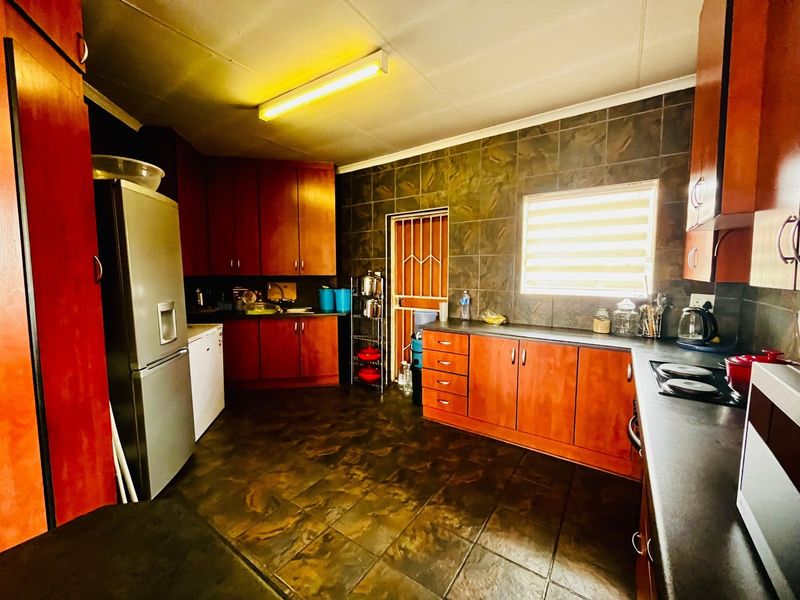 A functional kitchen featuring dark wood-look cabinetry, tiled backsplash, and dark floor tiles, providing a practical workspace with integrated hob and ample storage.