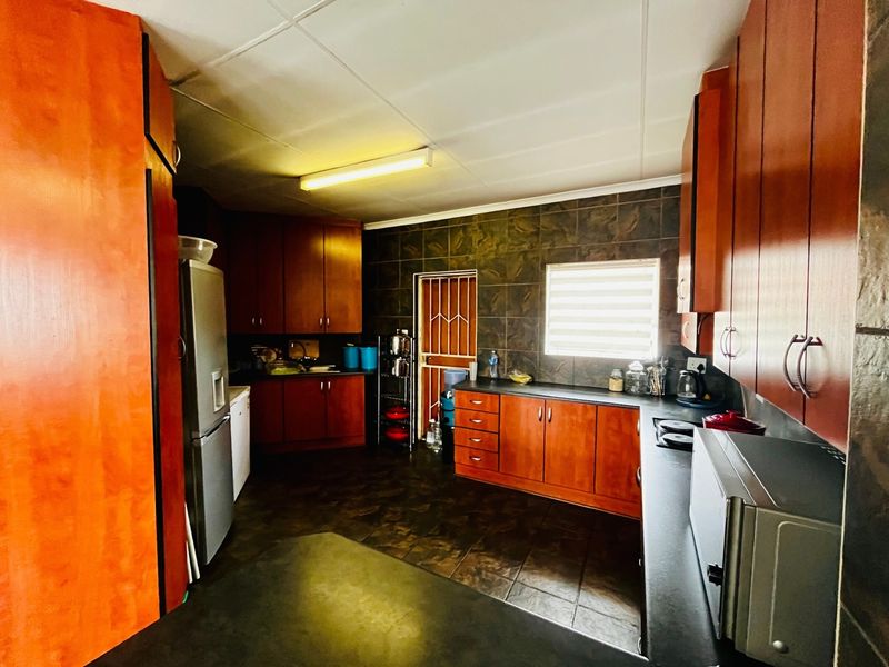 A functional kitchen featuring extensive wooden cabinetry, dark tiled flooring, and matching wall splashbacks, providing ample storage and workspace.