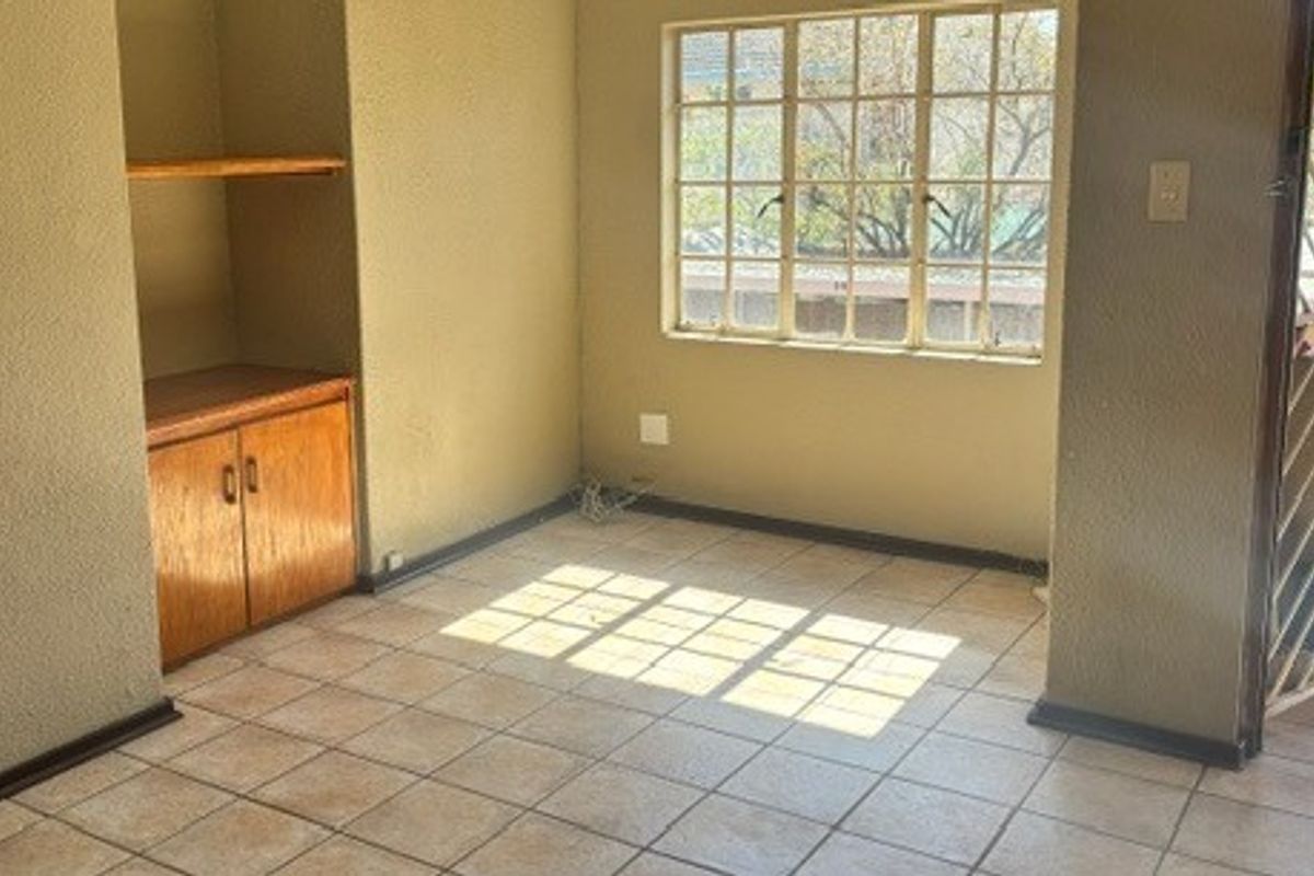 An empty living area featuring tiled flooring, built-in wooden cabinetry, and a security gate, offering a blank canvas for renovation.