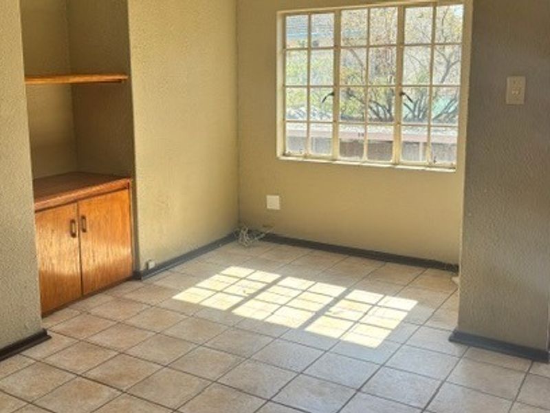 An empty living area featuring tiled flooring, built-in wooden cabinetry, and a security gate, offering a blank canvas for renovation.