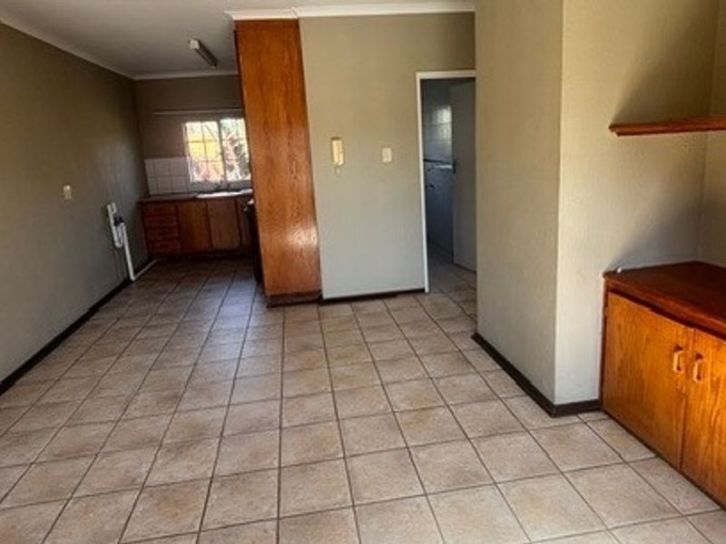 An open-plan living and kitchen area featuring tiled flooring, built-in wooden cabinetry, and an intercom system in a neutral, vacant space.