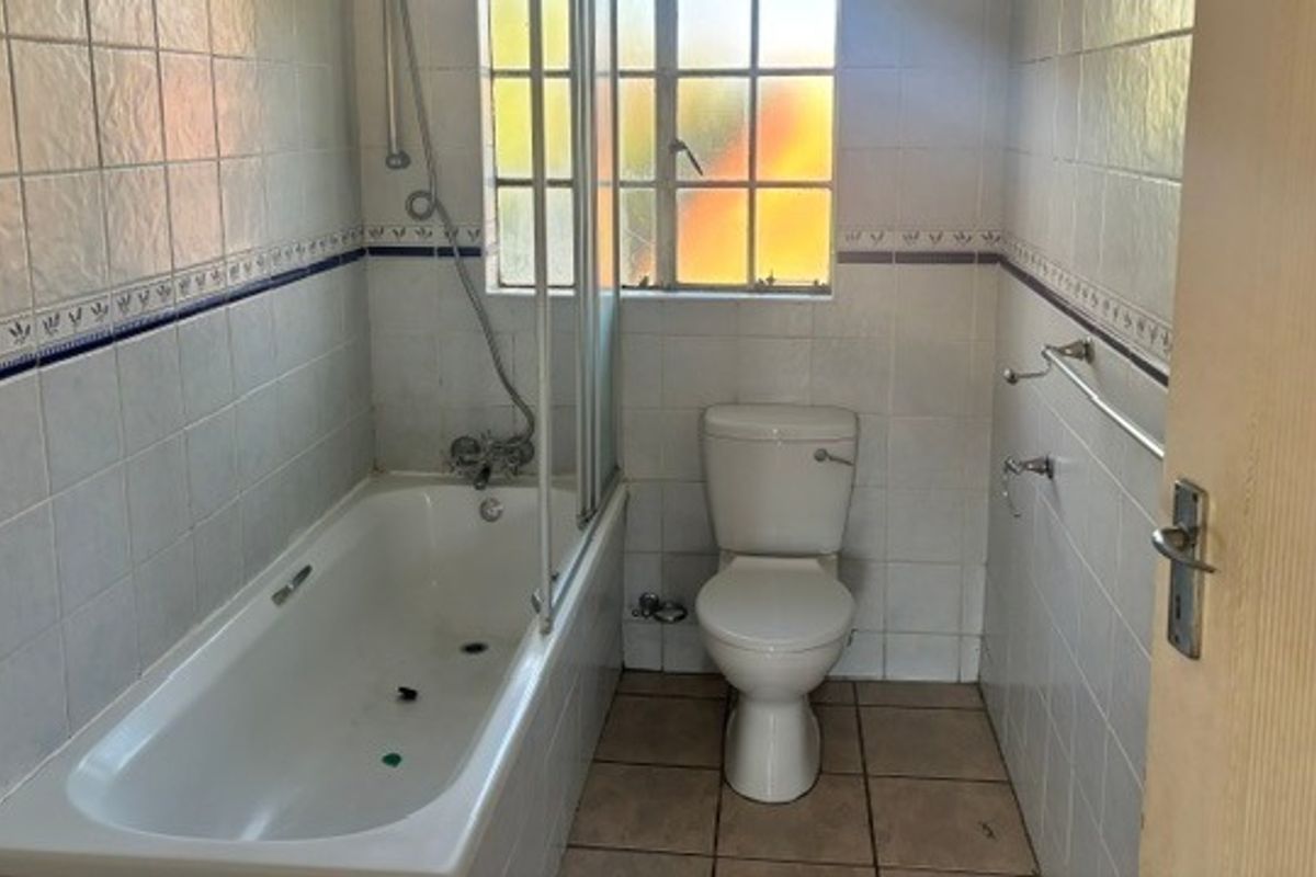 A functional bathroom featuring a bathtub with a glass shower screen, a standard toilet, and tiled finishes throughout.