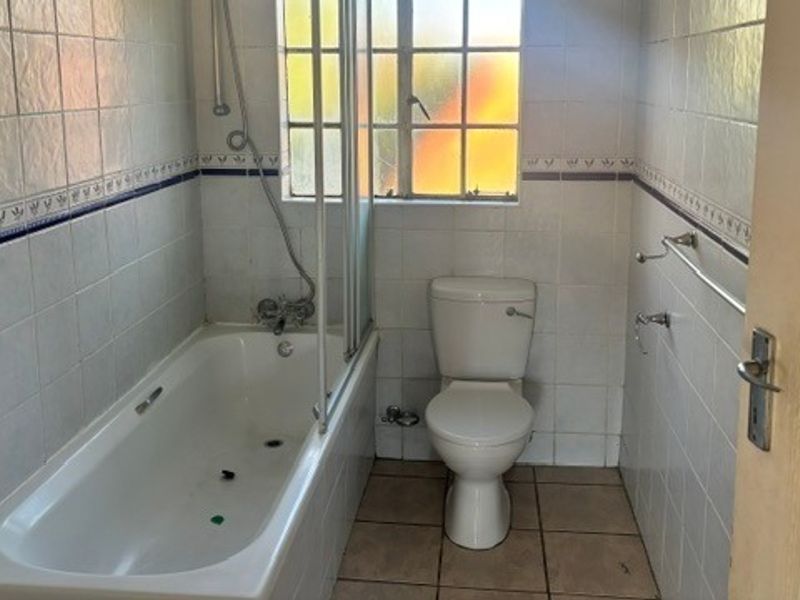 A functional bathroom featuring a bathtub with a glass shower screen, a standard toilet, and tiled finishes throughout.