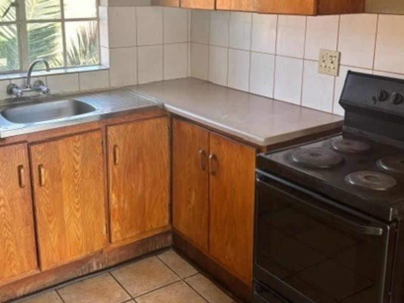 A functional kitchen featuring wooden cabinetry, a stainless steel sink, tiled backsplash, and an electric stove, offering potential for modern updates.