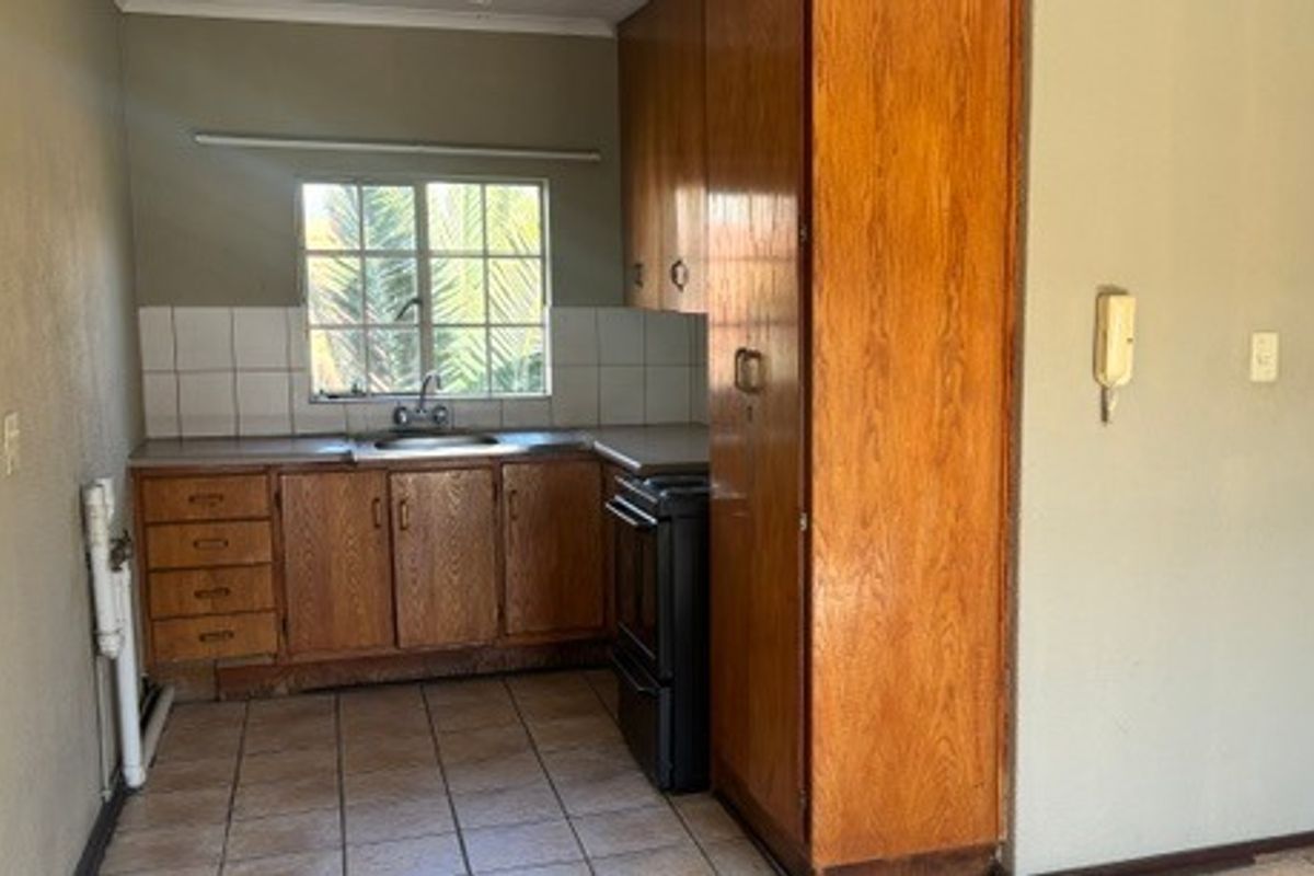 A functional kitchen featuring built-in wooden cabinetry, a stainless steel sink, tiled backsplash, and tiled flooring, offering a blank canvas for modern updates.