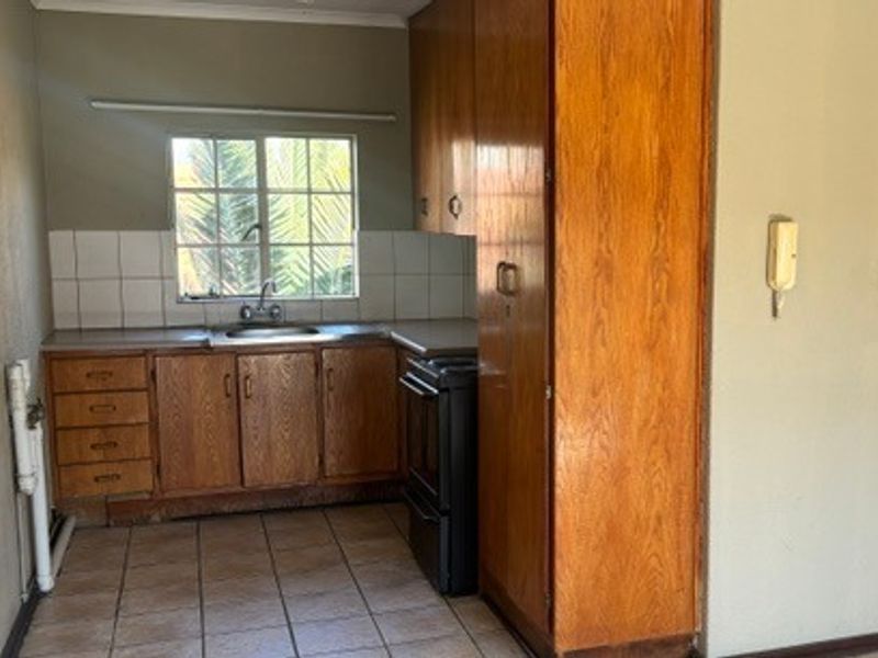 A functional kitchen featuring built-in wooden cabinetry, a stainless steel sink, tiled backsplash, and tiled flooring, offering a blank canvas for modern updates.