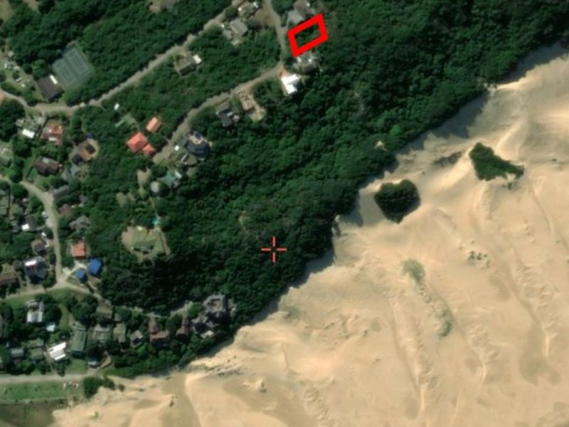 Aerial view of a residential plot located in a coastal area, surrounded by dense vegetation and adjacent to sand dunes.
