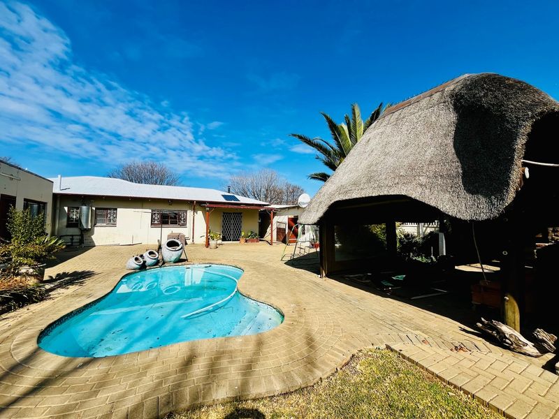 Outdoor entertainment area featuring a swimming pool and a traditional thatch-roof lapa set within a paved courtyard.