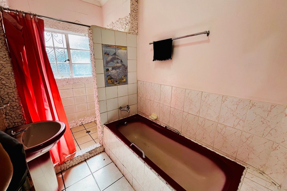 A dated bathroom featuring a pedestal basin, built-in bathtub, and tiled shower area with decorative wall tiles and security window bars.