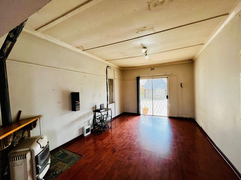 Spacious living area featuring laminate flooring, a sliding door with security gate, and a fireplace hearth, requiring cosmetic updates to the ceiling and walls.