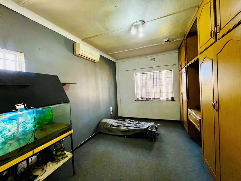 A bedroom featuring built-in wooden cupboards, a split-system air conditioner, and window blinds, requiring cosmetic updates to the ceiling and flooring.