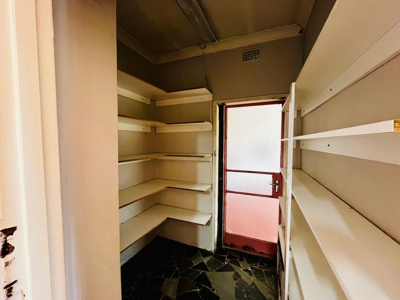 A functional scullery or pantry area featuring extensive built-in shelving, tiled flooring, and direct access to the exterior.