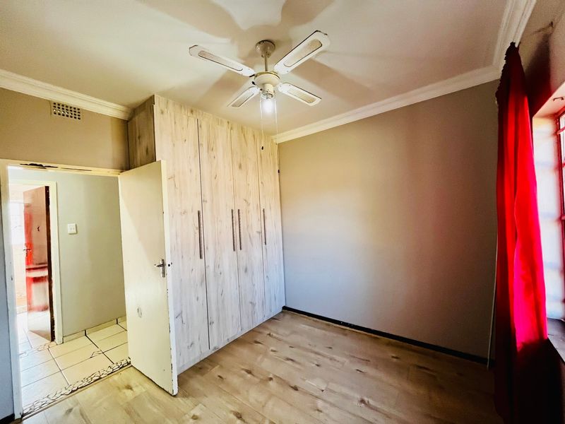 A bright, empty bedroom featuring light wood-look laminate flooring, built-in cupboards, and a ceiling fan, offering a clean and neutral space.