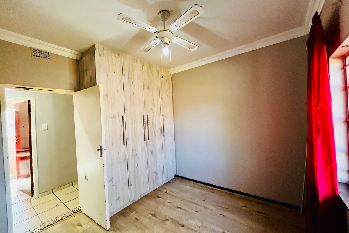 A bright, empty bedroom featuring light wood-look laminate flooring, built-in cupboards, and a ceiling fan, offering a clean and neutral space.