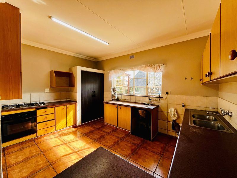 A functional kitchen featuring wooden cabinetry, a gas hob, built-in oven, and double bowl sink with tiled flooring and splashbacks.