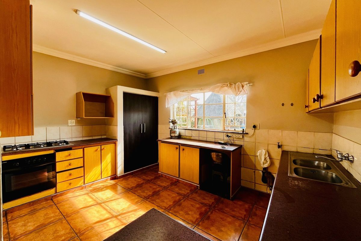 A functional kitchen featuring wooden cabinetry, a gas hob, built-in oven, and double bowl sink with tiled flooring and splashbacks.
