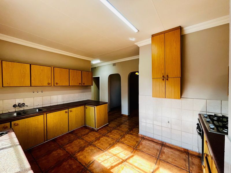 A functional kitchen featuring wooden cabinetry, tiled splashbacks, a built-in gas hob, and ceramic floor tiles, offering a clean and practical layout.