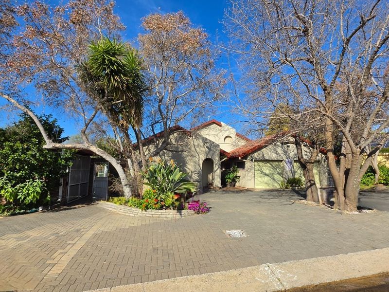 Front exterior view of the house featuring a paved driveway, double garage, and established garden with mature trees.