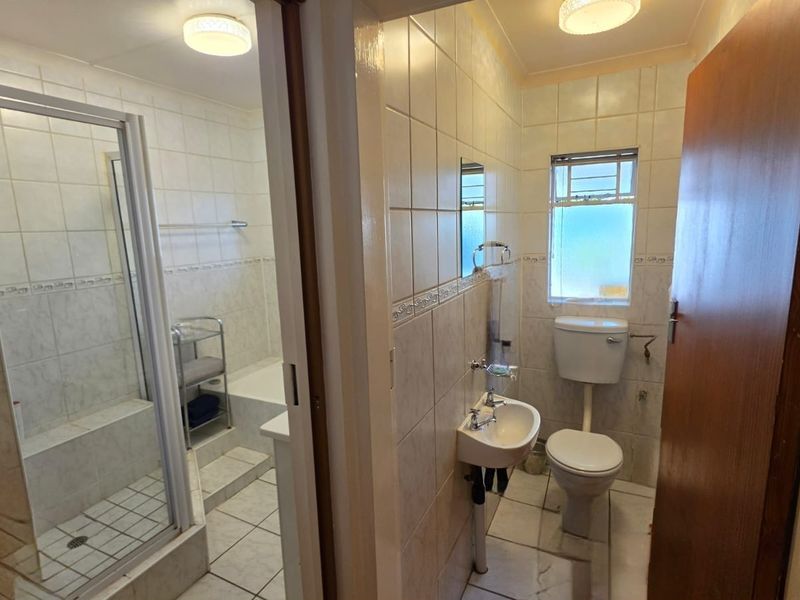 A functional bathroom featuring a separate shower enclosure, pedestal basin, and toilet with neutral tiled finishes throughout.
